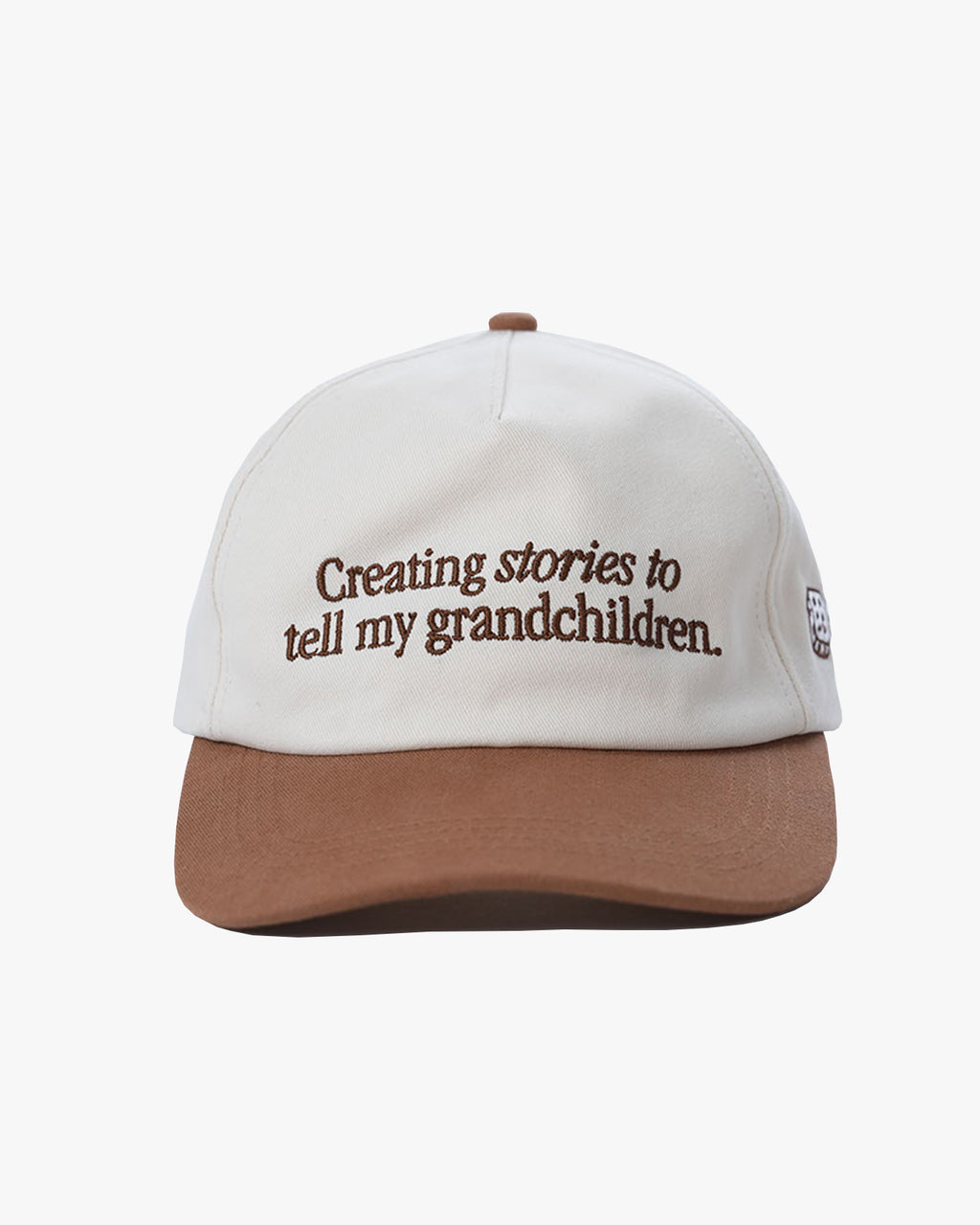 White cap with brown brim and text 'Creating stories to tell my grandchildren' with 'dobbel' on the back of the cap