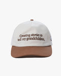 White cap with brown brim and text 'Creating stories to tell my grandchildren' with 'dobbel' on the back of the cap