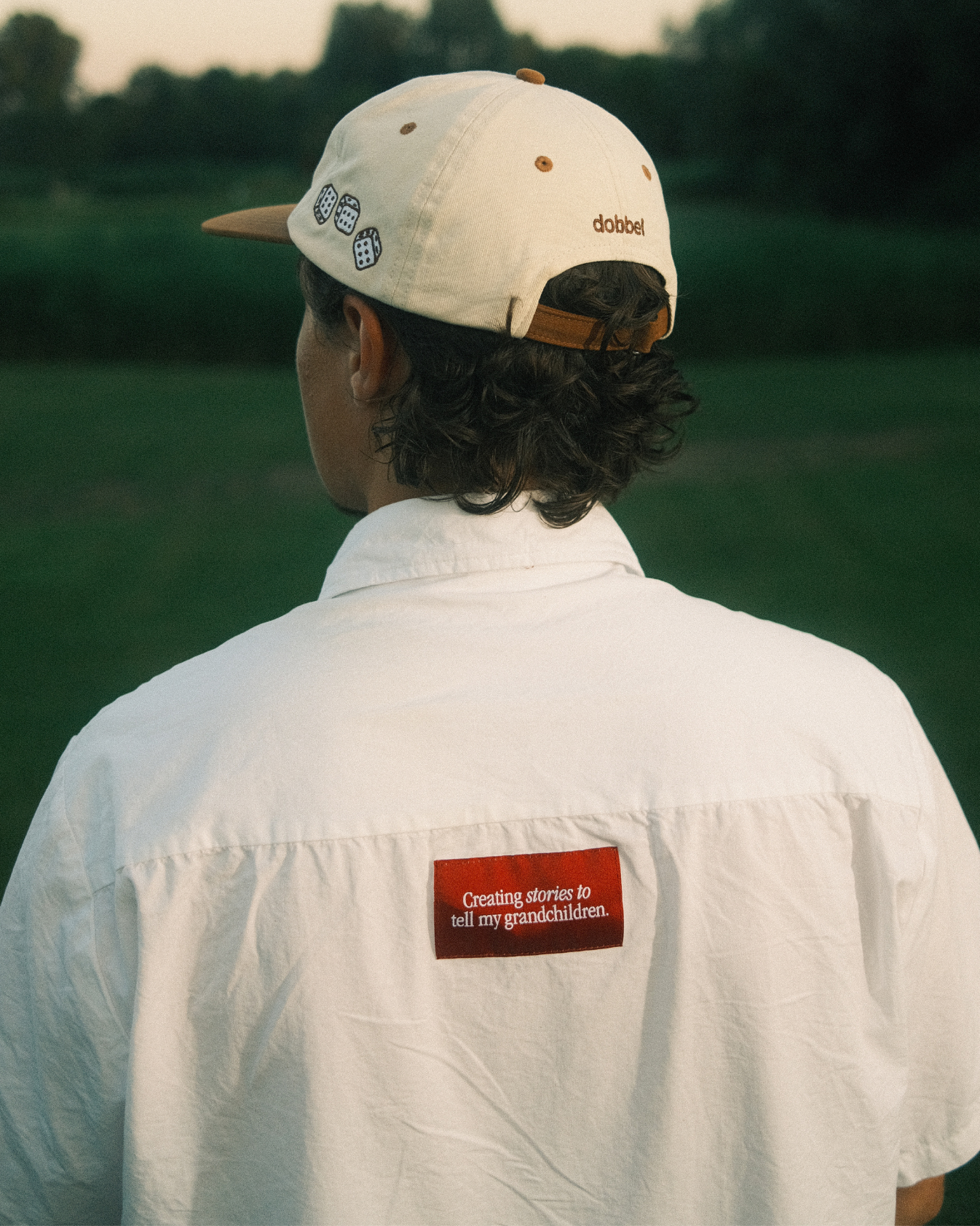 Man wearing a white dobbel cap and shirt with a visible dobbel brand logo, standing in a field.