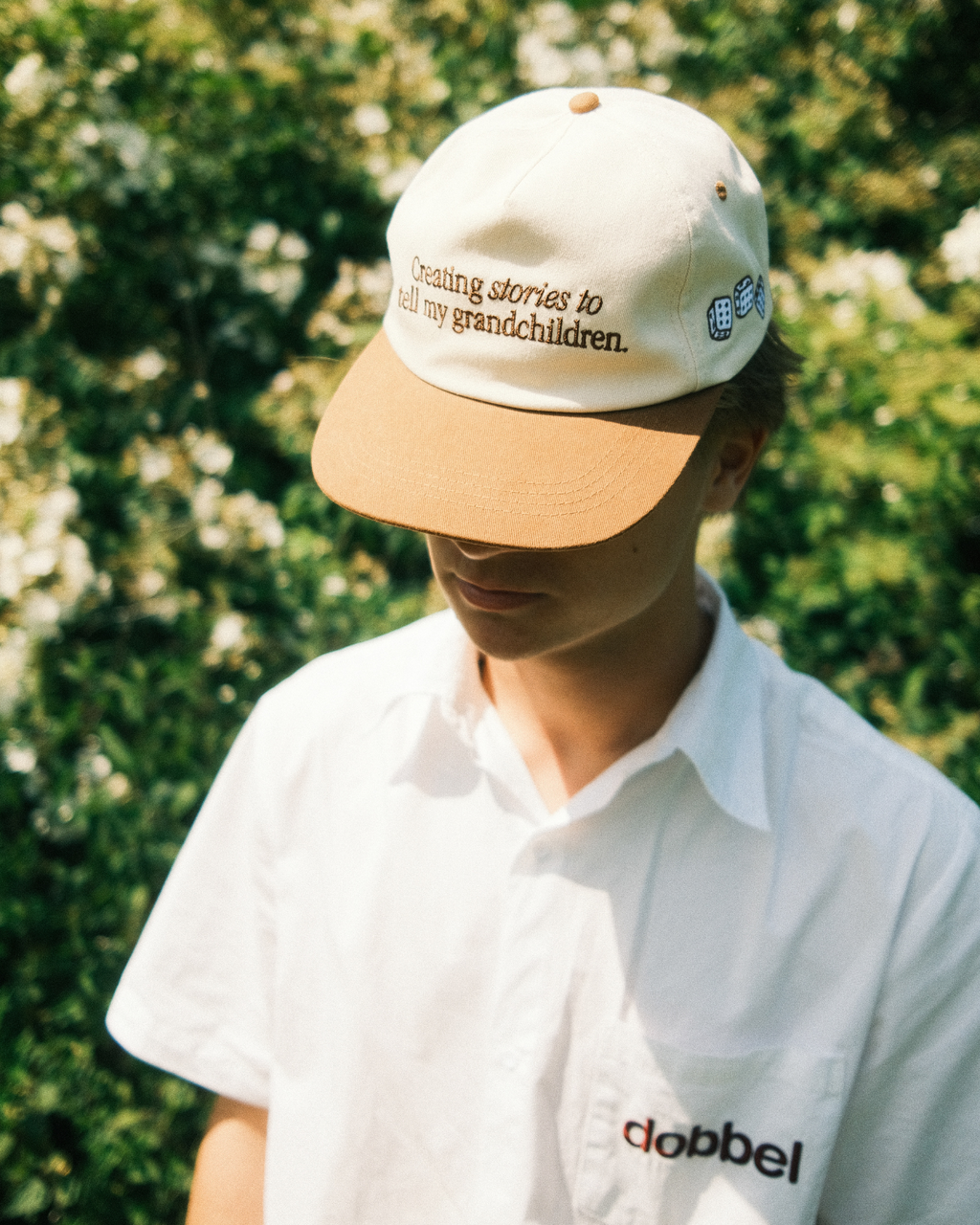Person wearing a beige and white cap with text, standing against a green leafy background