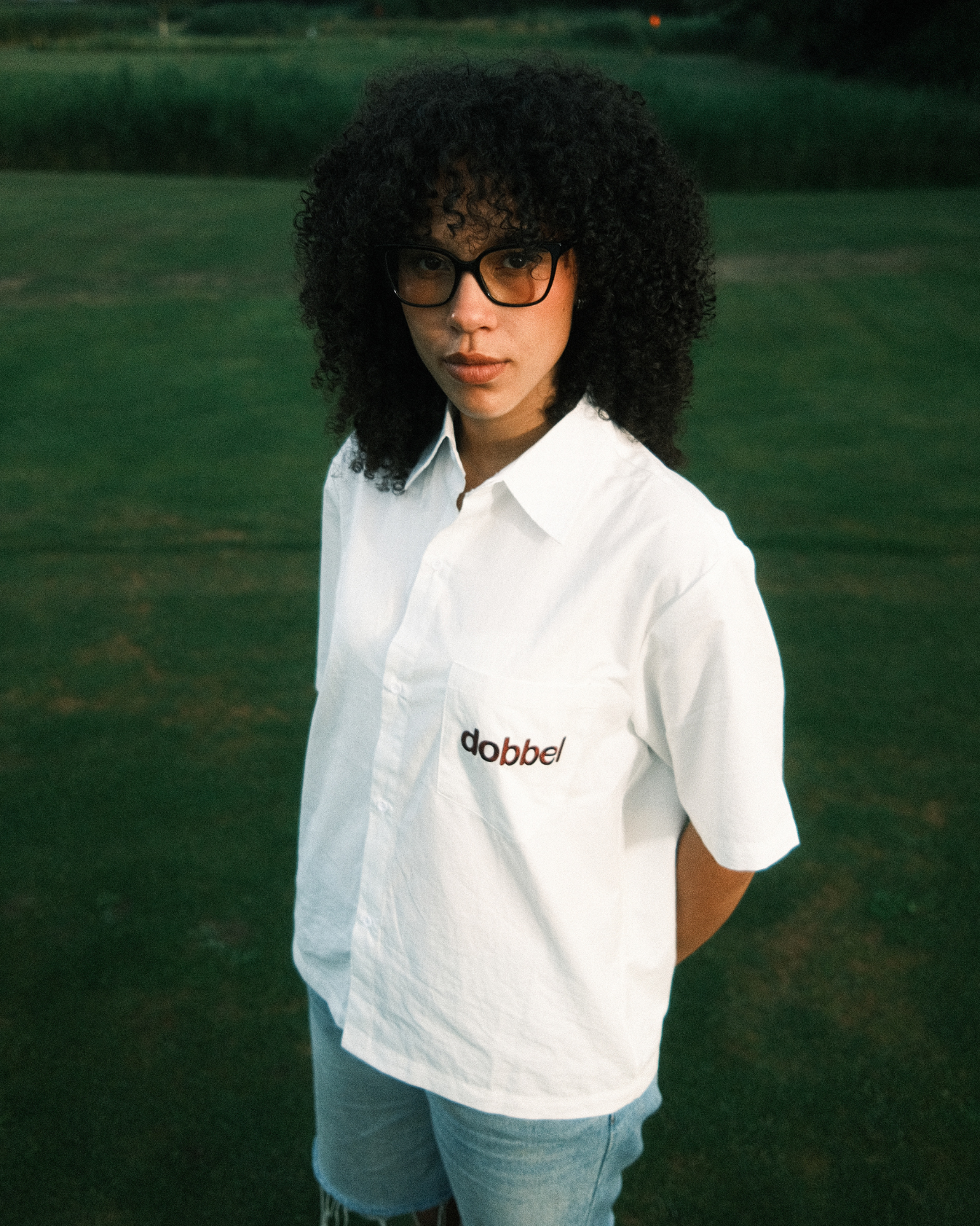 Woman wearing a white shirt with 'dobbel' logo in a grassy field